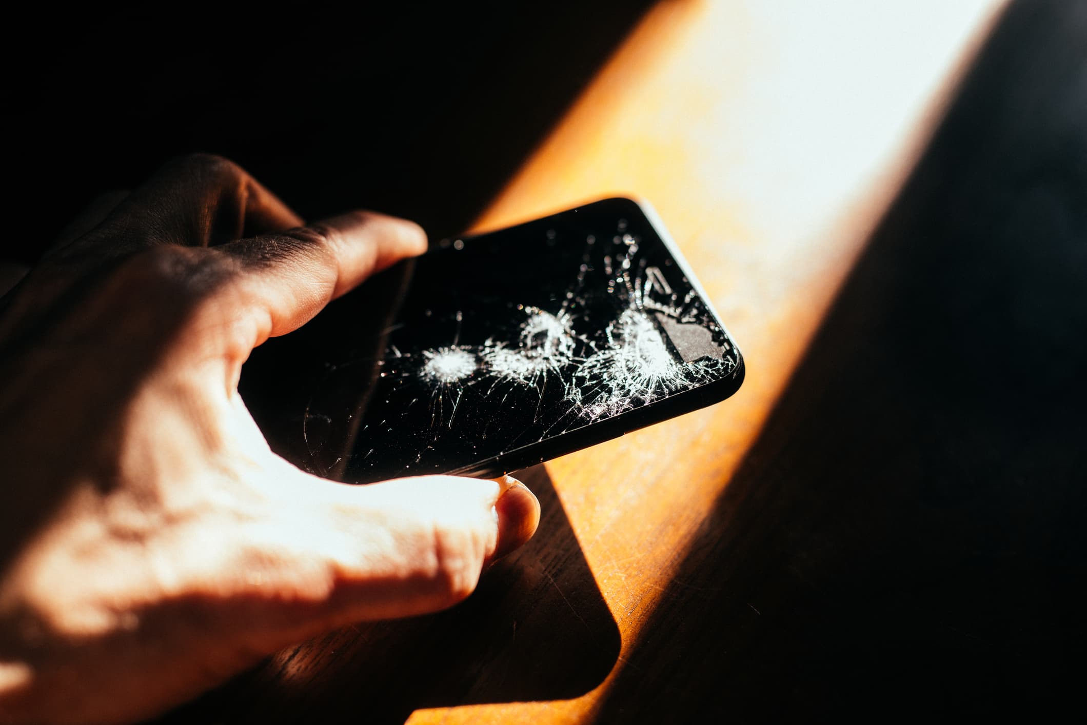 Hand holding damaged mobile phone in light beam.